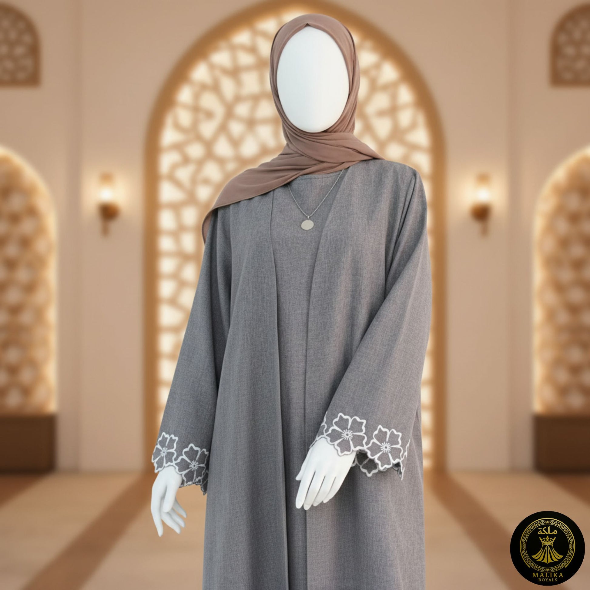 Gray abaya with floral lace cuffs on against an ornate middle eastern archway.