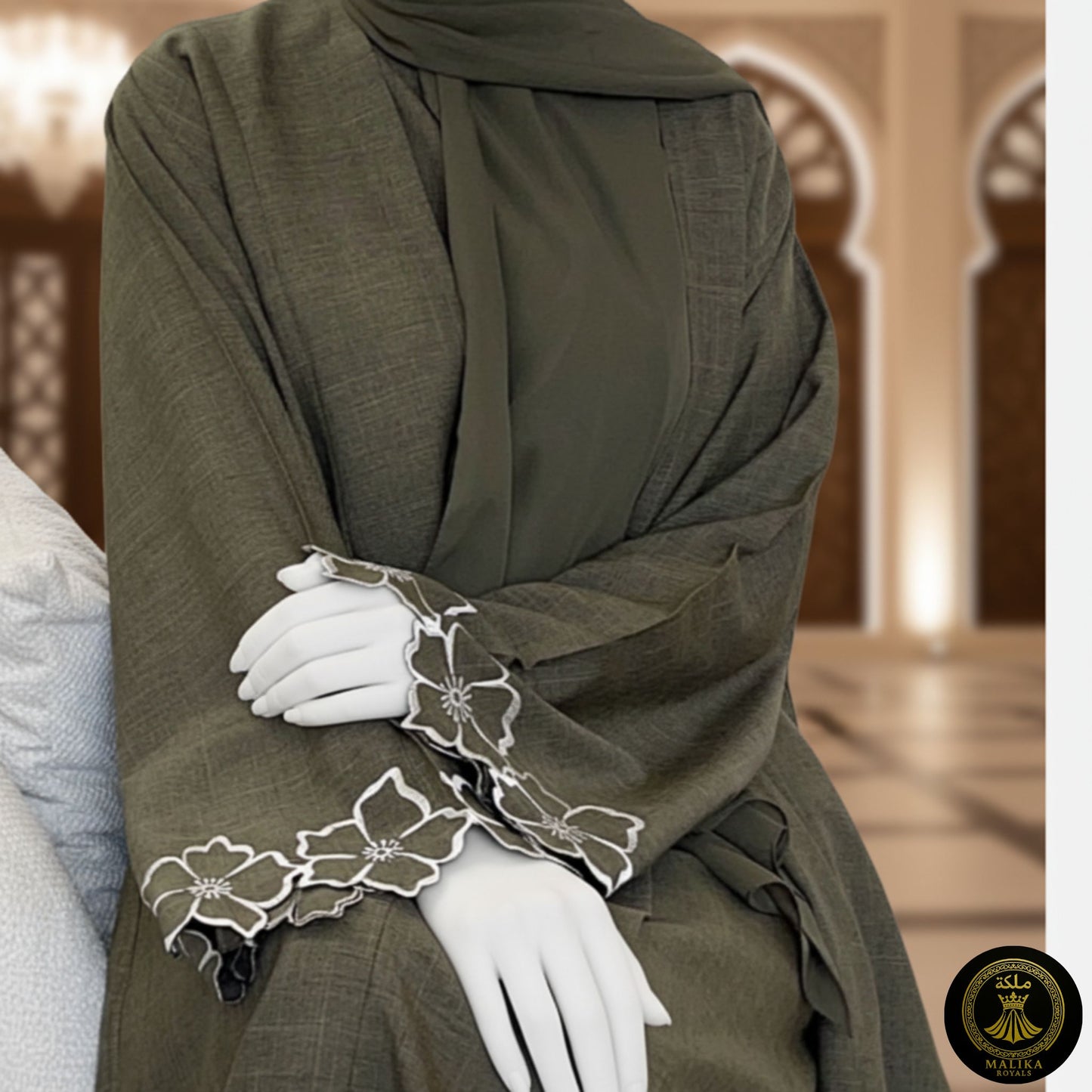Person wearing a luxury dark green abaya with white floral embroidery in a decorated interior setting