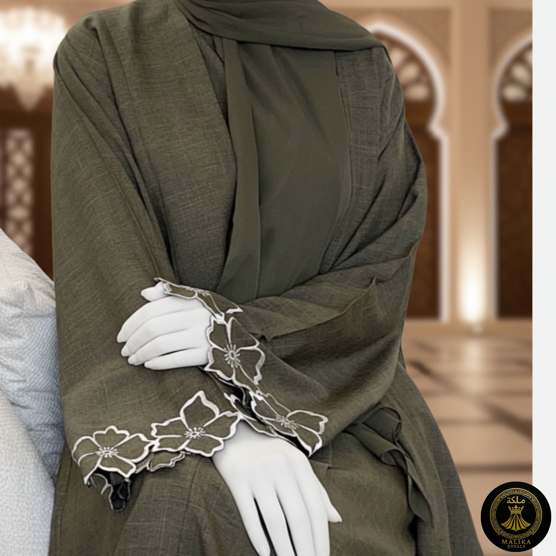 Person wearing a luxury dark green abaya with white floral embroidery in a decorated interior setting