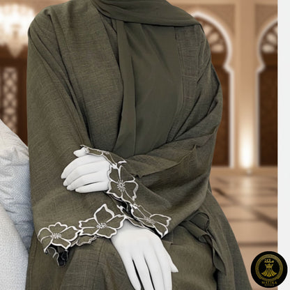 Person wearing a luxury dark green abaya with white floral embroidery in a decorated interior setting