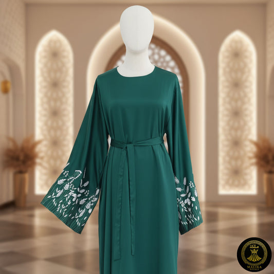 Green dress with floral embroidery on sleeves on a mannequin against an ornate wall.
